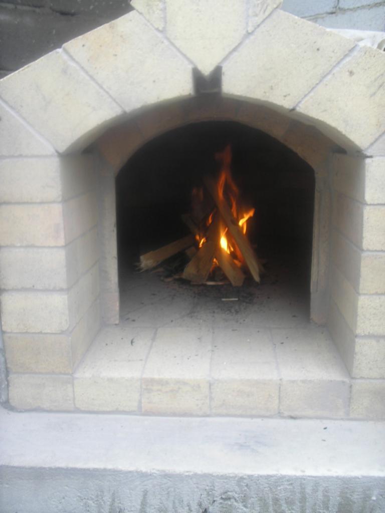 Murowany piec z palącym się drewnem wewnątrz, widoczne szare cegły i płomienie