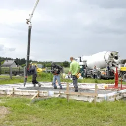 Wylewanie betonu na przygotowany fundament z rurami grzewczymi w Piekary Śląskie, widoczna pompa do betonu i betoniarka.