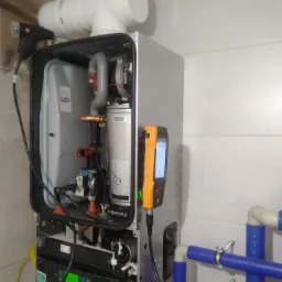 Kocioł grzewczy z podłączonymi rurami wodnymi w kolorze niebieskim i czerwonym, sprawdzany za pomocą dwóch urządzeń pomiarowych marki Testo i Buderus.