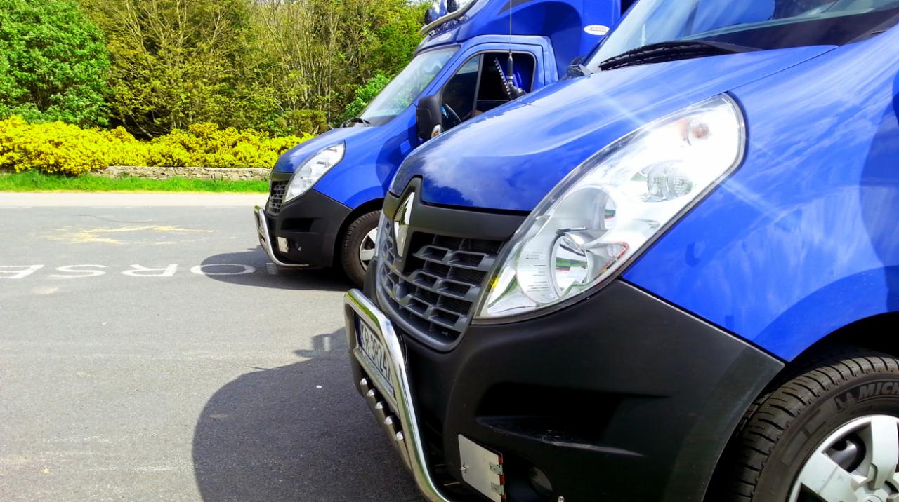 Dwa niebieskie busy Renault Master zaparkowane na asfaltowej drodze z widocznymi napisami 'HORSE', z chromowanymi orurowaniami z przodu, na tle zieleni i żółtych krzewów.