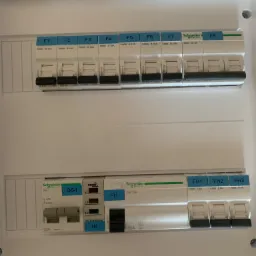 Rozdzielnica elektryczna z widocznymi bezpiecznikami i oznaczeniami producenta Schneider Electric, widok z bliska.