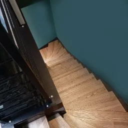 Wewnętrzne schody z jesionowymi stopniami, widok z góry, metalowa balustrada, ściana w kolorze morskim.