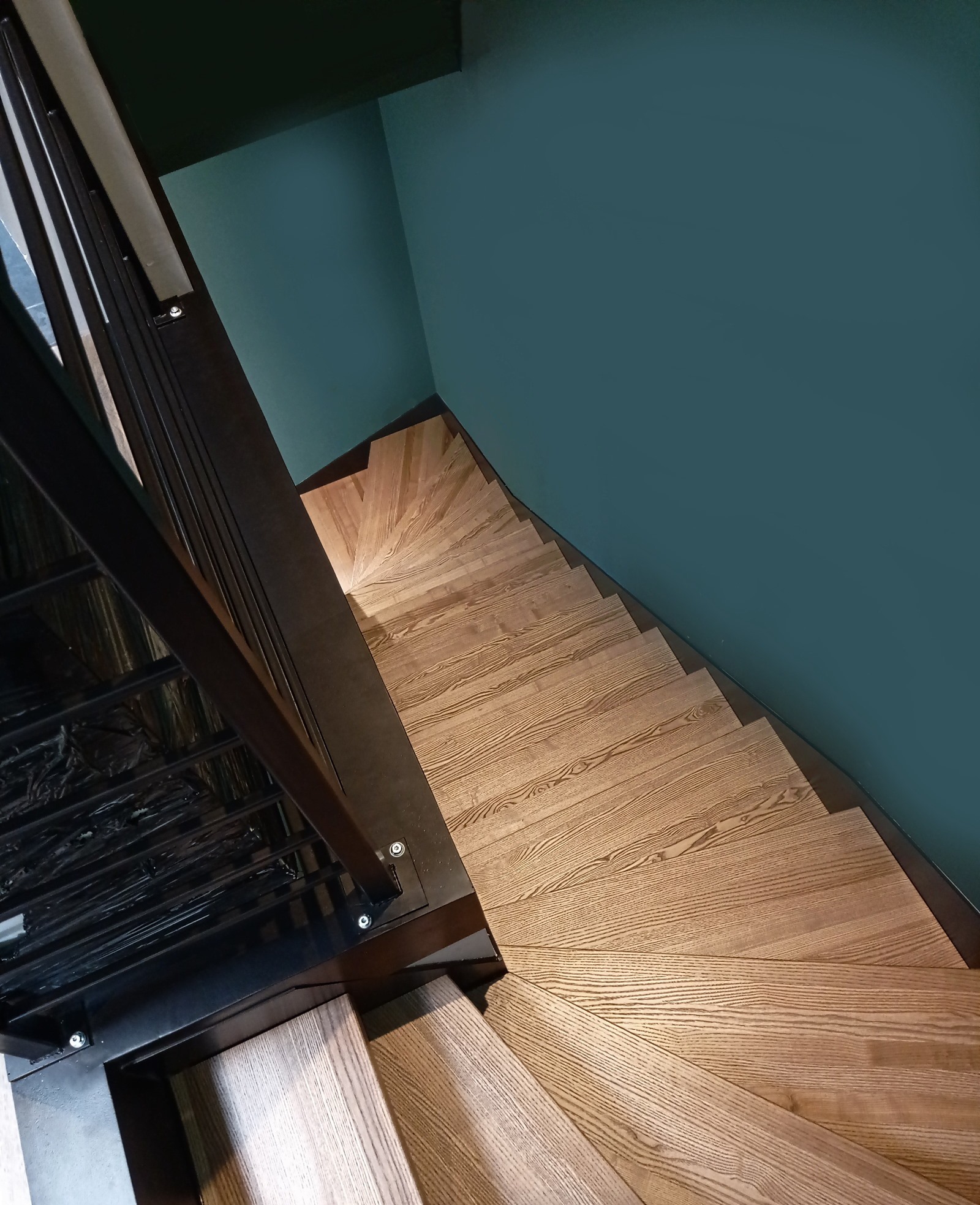 Wewnętrzne schody z jesionowymi stopniami, widok z góry, metalowa balustrada, ściana w kolorze morskim.