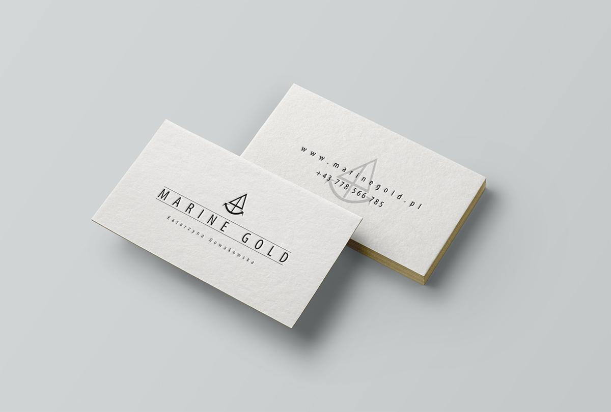 Dwie wizytówki firmy Marine Gold z Kalwarii Zebrzydowskiej, z minimalistycznym logo przedstawiającym żaglówkę, na jasnoszarym tle. Jedna wizytówka leży płasko, a druga jest ustawiona pod kątem...