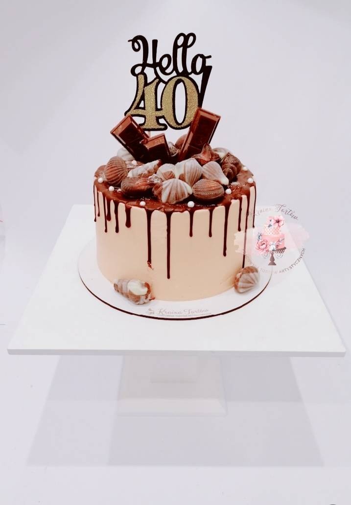 Tort urodzinowy z czekoladowymi dekoracjami, polewą i napisem 'Hello 40' na białym tle.