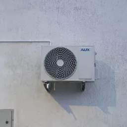 Zewnętrzna jednostka klimatyzatora AUX zamontowana na szarej, chropowatej ścianie budynku, widoczne mocowania i fragment instalacji.