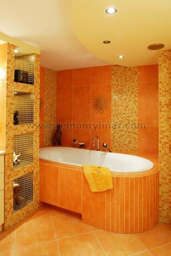 Pomarańczowa łazienka z zabudowaną wanną, mozaiką na ścianach i półkami wnękowymi, oświetlona punktowymi lampami sufitowymi, z żółtym ręcznikiem na wannie.