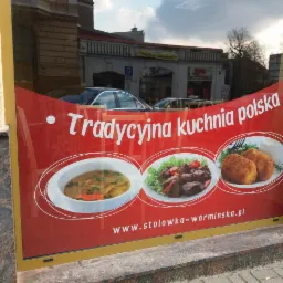 Czerwony baner reklamowy w oknie lokalu gastronomicznego z hasłem 'Tradycyjna kuchnia polska' i zdjęciami zupy, mięsa i kotletów, odbicia ulicy w szybie.