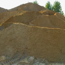 G&oacute;ra piasku z wyraźnymi śladami opon pojazdu budowlanego, w tle zieleń drzew.