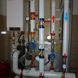 Kompaktowa kotłownia gazowa z białym kotłem wiszącym Viessmann, zbiornikiem akumulacyjnym i rozbudowanym systemem rur z zaworami, manometrami i pompami obiegowymi LFP, oznaczonymi strzałkami...