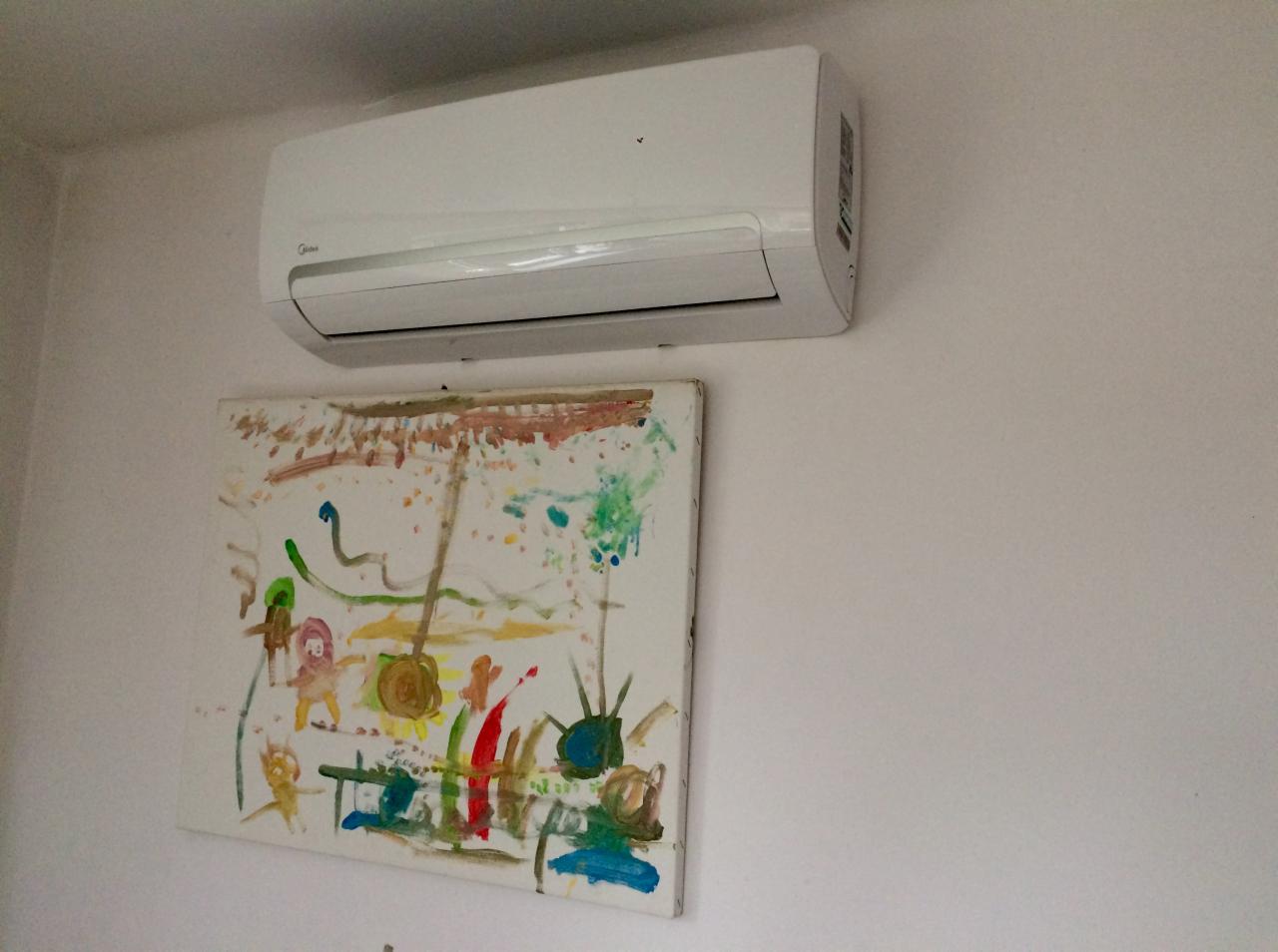 Biały klimatyzator Midea zamontowany na ścianie nad dziecięcym obrazkiem.