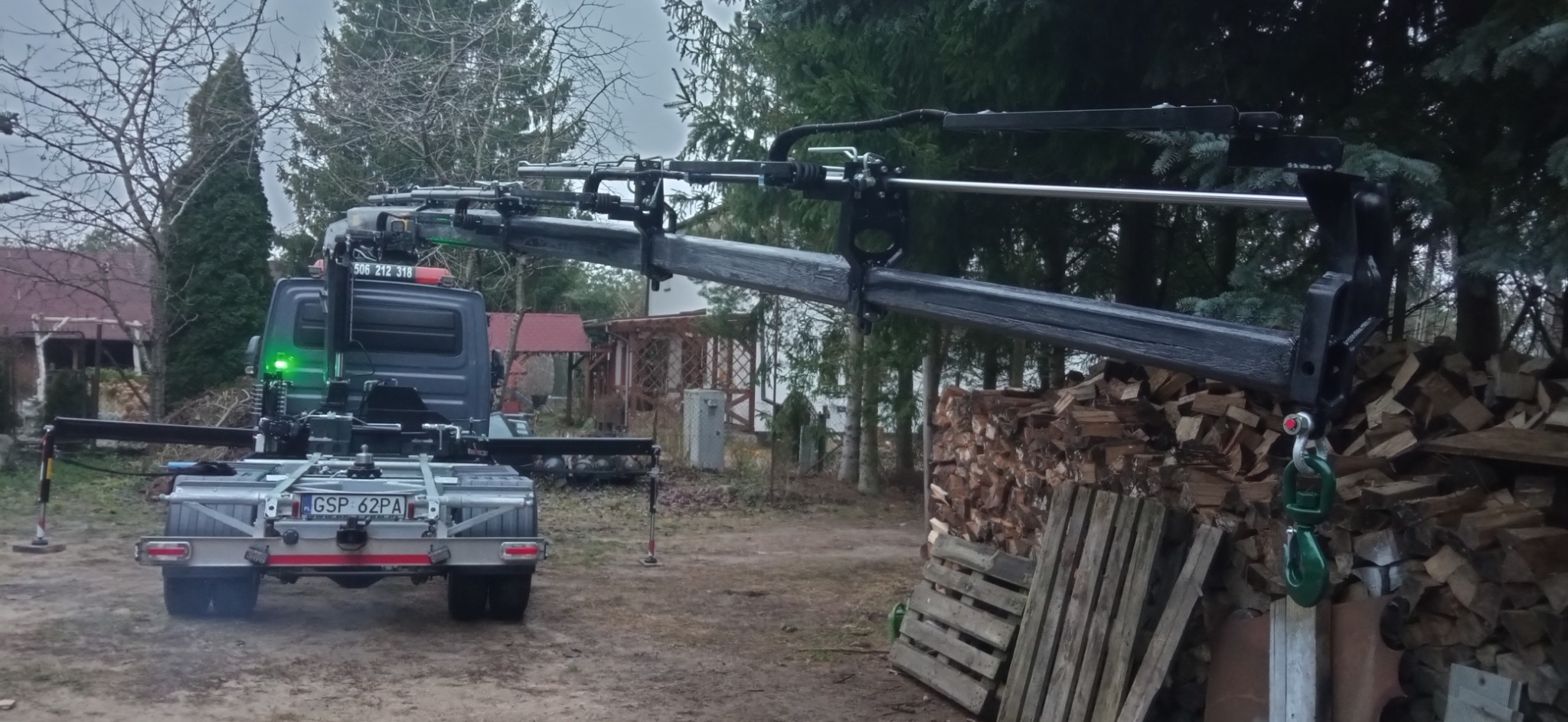 Samochód z dźwigiem HDS na posesji, obok stos drewna. Widoczne podpory stabilizujące pojazd. Tablica rejestracyjna GSP 62PA.