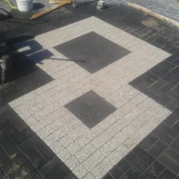 Dwukolorowa kostka brukowa ułożona we wzór z kwadratami w Rychowie, widoczne narzędzia i wiadro z zaprawą.