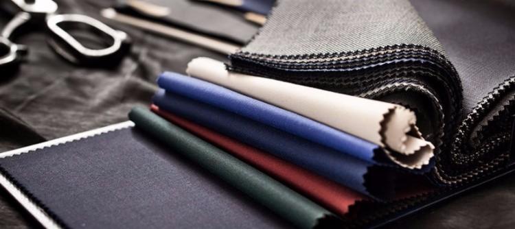 Próbki tkanin w różnych kolorach i fakturach, ułożone obok siebie, z nożyczkami krawieckimi w tle.