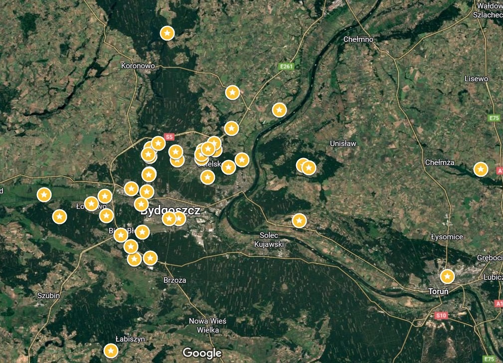 Mapa satelitarna okolic Bydgoszczy z naniesionymi pinezkami, prawdopodobnie lokalizacjami firm lub punktów usługowych. Widoczne lasy, pola uprawne i rzeka Wisła.