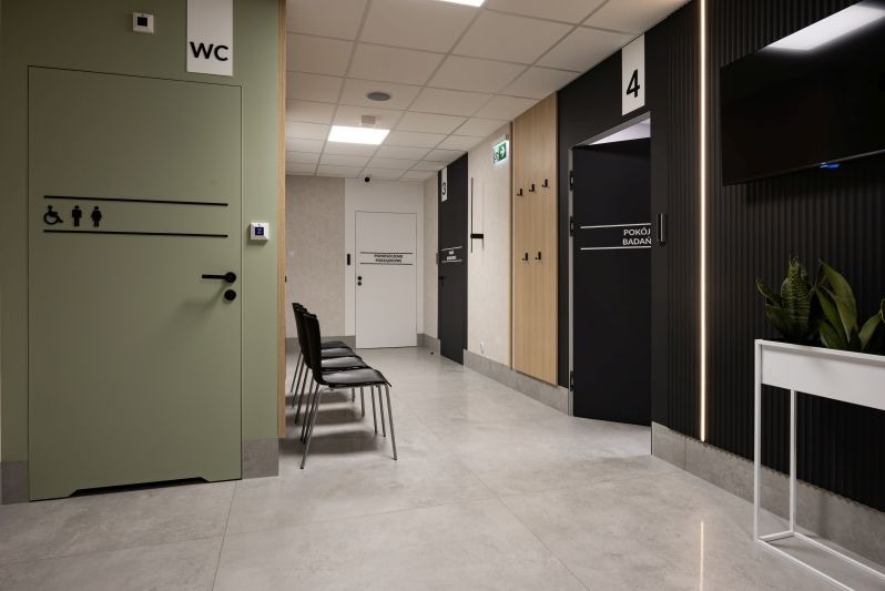 Korytarz w nowoczesnym budynku medycznym z drzwiami do WC, pokojów badań i poczekalnią z krzesłami. Minimalistyczny design, stonowana kolorystyka, oświetlenie LED.