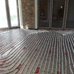 Białe rurki ogrzewania podłogowego ułożone na czerwonej siatce w nowym budynku z dużymi oknami i kamienną kolumną.