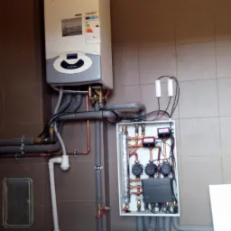 Zamontowany gazowy kocioł kondensacyjny z podłączonymi instalacjami, widoczna szafka sterująca z pompami obiegowymi na brązowych rurach miedzianych.