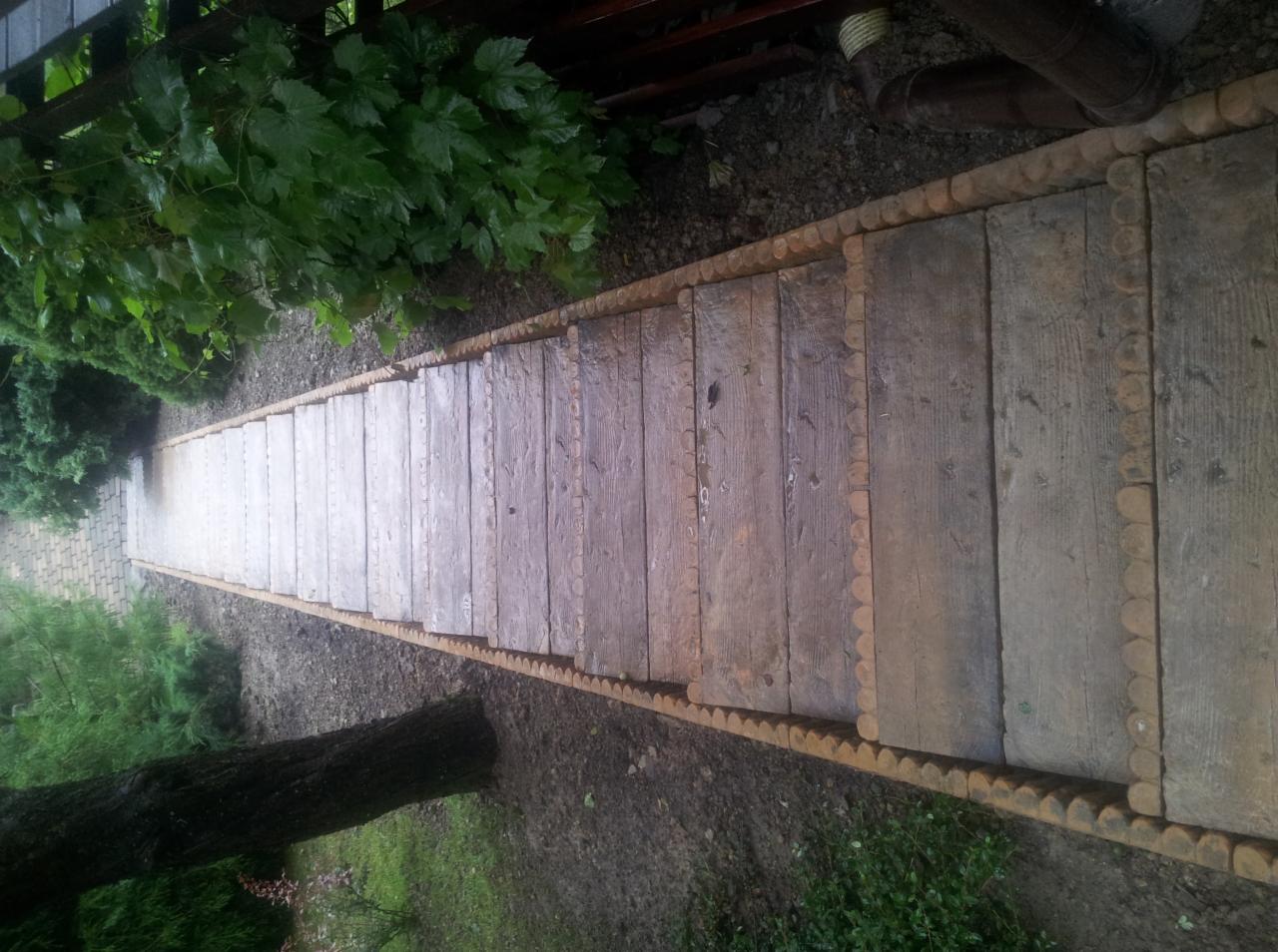 Długie, drewniane schody ogrodowe z ozdobnymi krawędziami z okrąglaków, prowadzące w dół zbocza, otoczone zielenią.