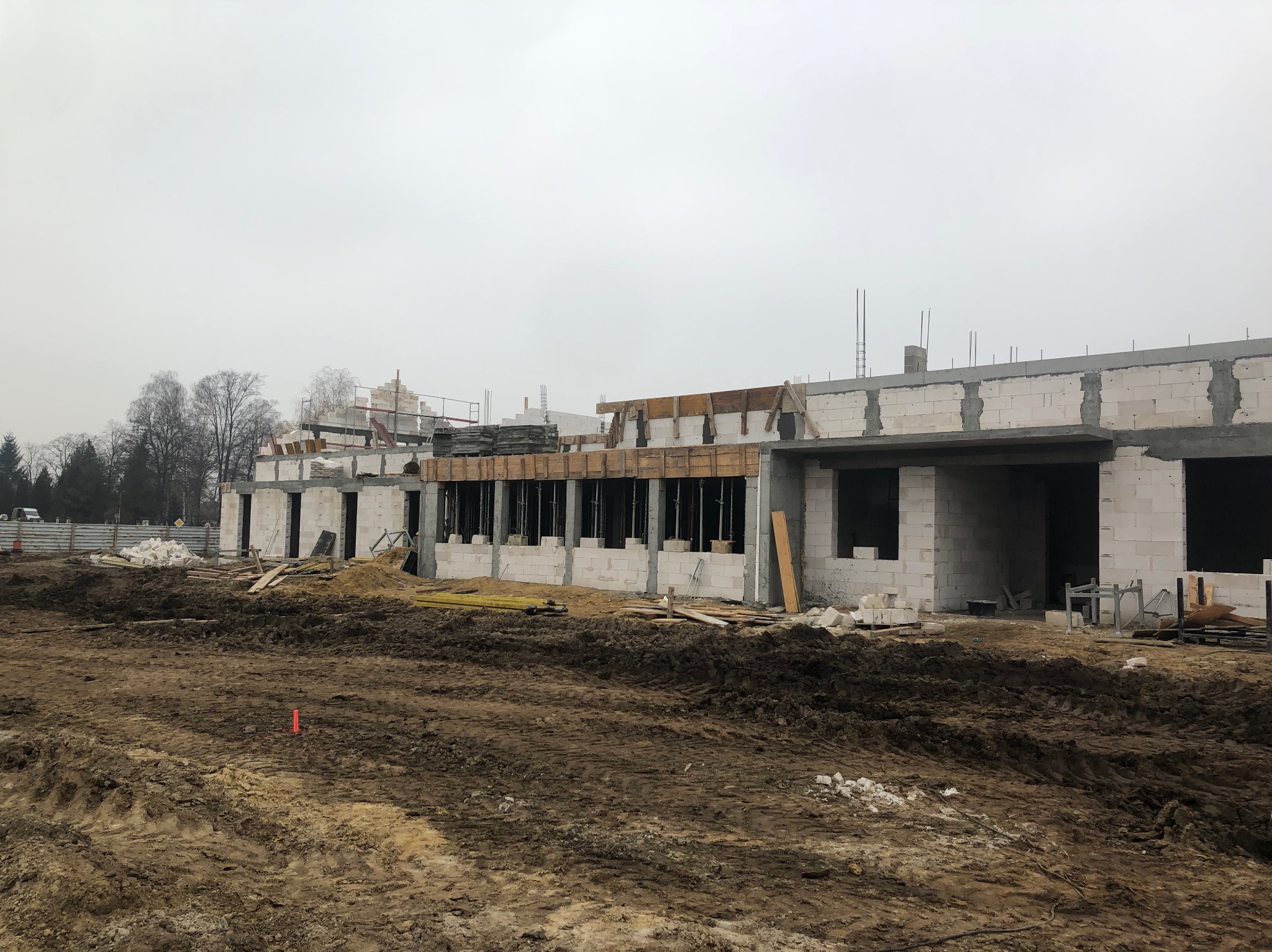 Budowa domu w trakcie: wzniesione ściany z betonu komórkowego, widoczne zbrojenia i szalunki, przygotowany teren. Pochmurny dzień.