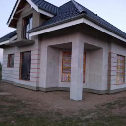 Fhu Izabela - Surowy stan elewacji domu jednorodzinnego z oknami zabezpieczonymi folią, przygotowany do dalszych prac wykończeniowych.