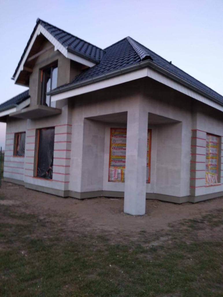 Surowy stan elewacji domu jednorodzinnego z oknami zabezpieczonymi folią, przygotowany do dalszych prac wykończeniowych.