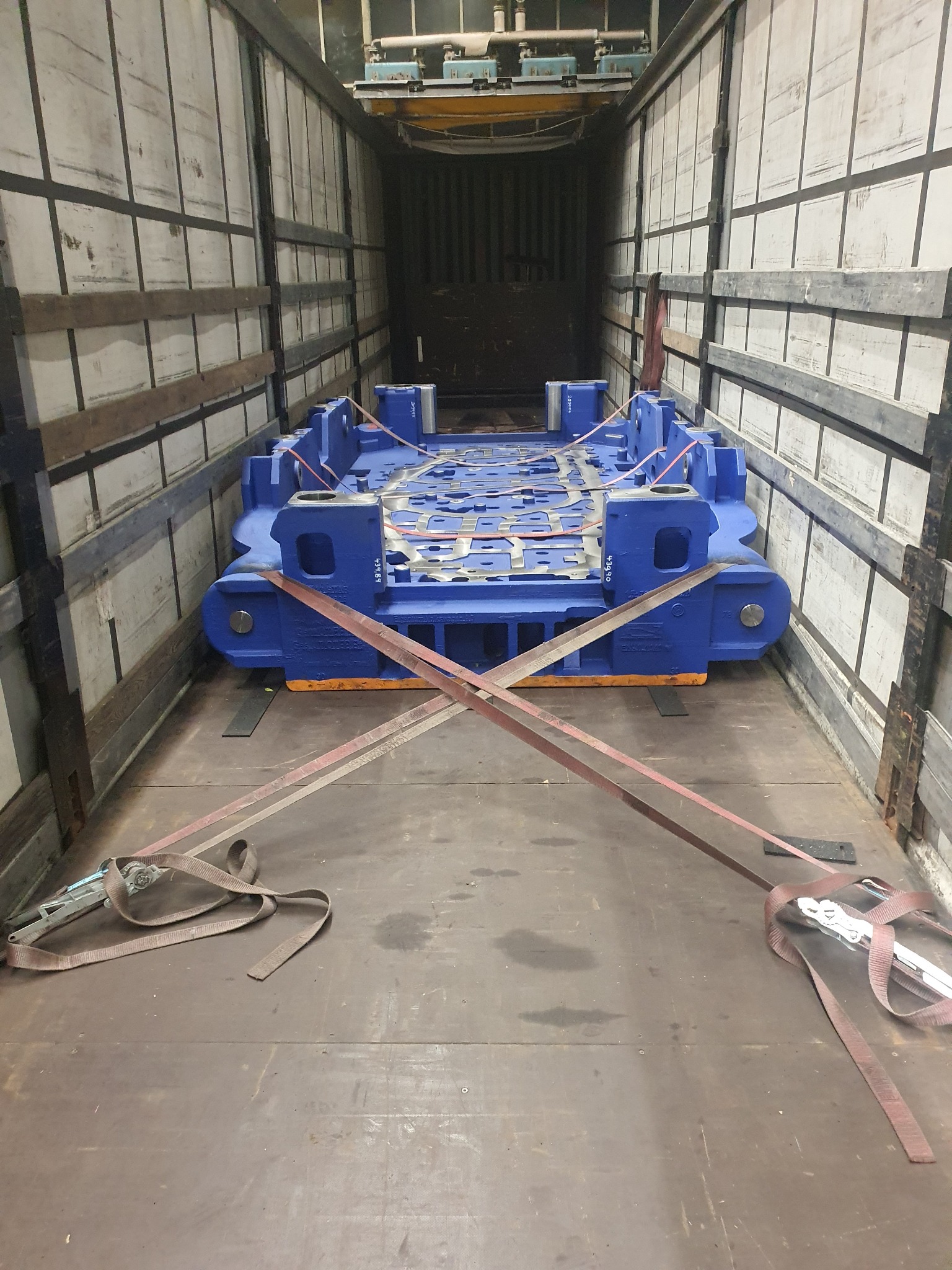 Niebieska matryca do wytłaczania karoserii samochodowych, zabezpieczona pasami transportowymi, umieszczona wewnątrz naczepy ciężarówki z rozsuwanym dachem.