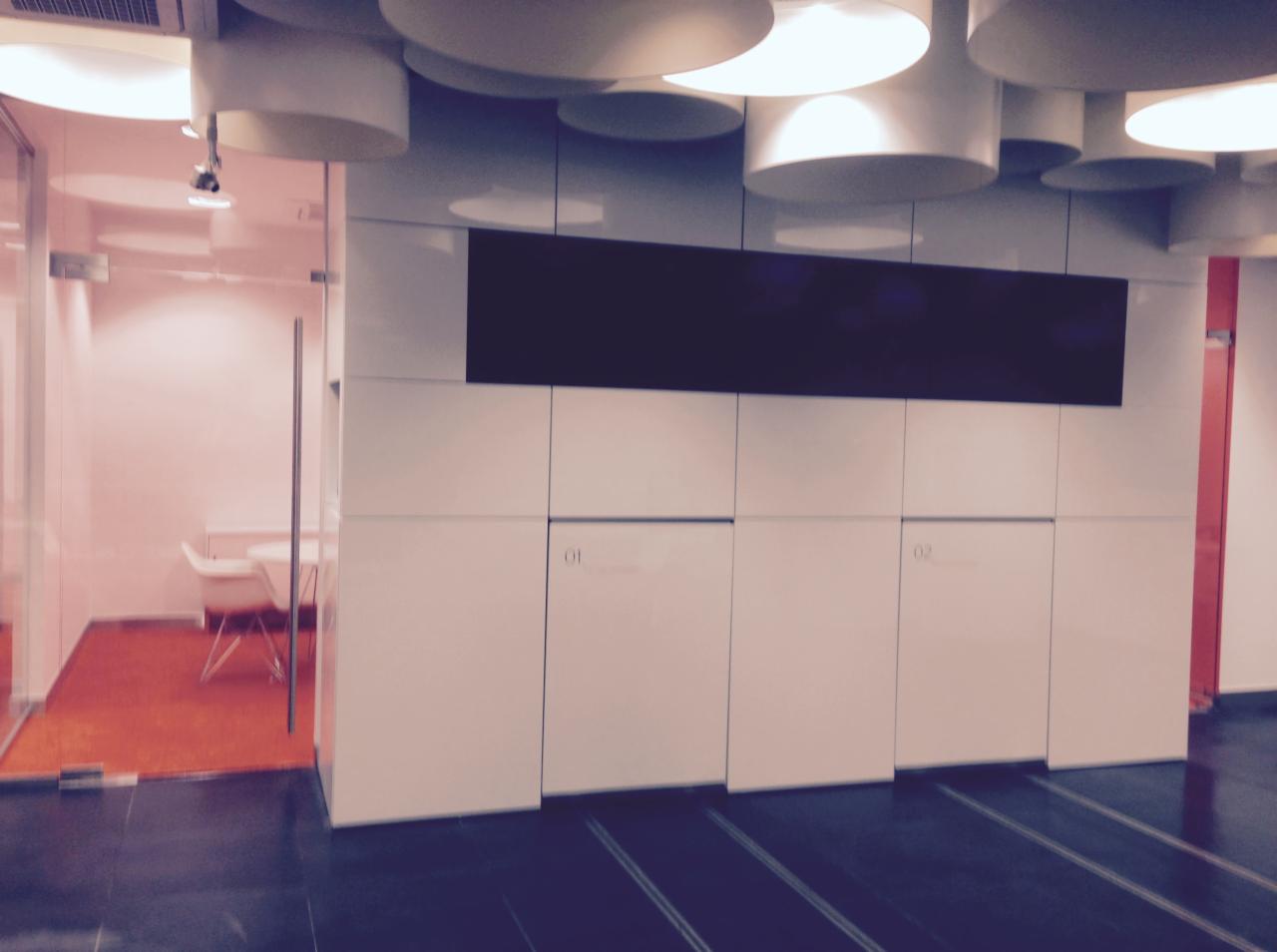 Nowoczesne biuro z przeszkloną salą konferencyjną, białą zabudową meblową z numerami '01' i '02', oraz okrągłymi lampami sufitowymi.