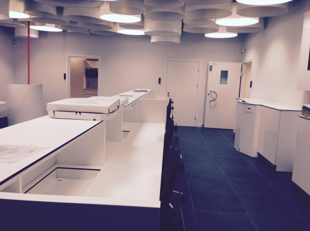 Nowoczesne wnętrze biurowe z podwieszanym sufitem z okrągłych lamp, białą ladą recepcyjną z pudełkami i ciemną podłogą z płytek.