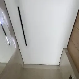 Biały, matowy sufit napinany z czarnym, liniowym oświetleniem LED w nowoczesnej łazience z beżowymi ścianami i lustrem.