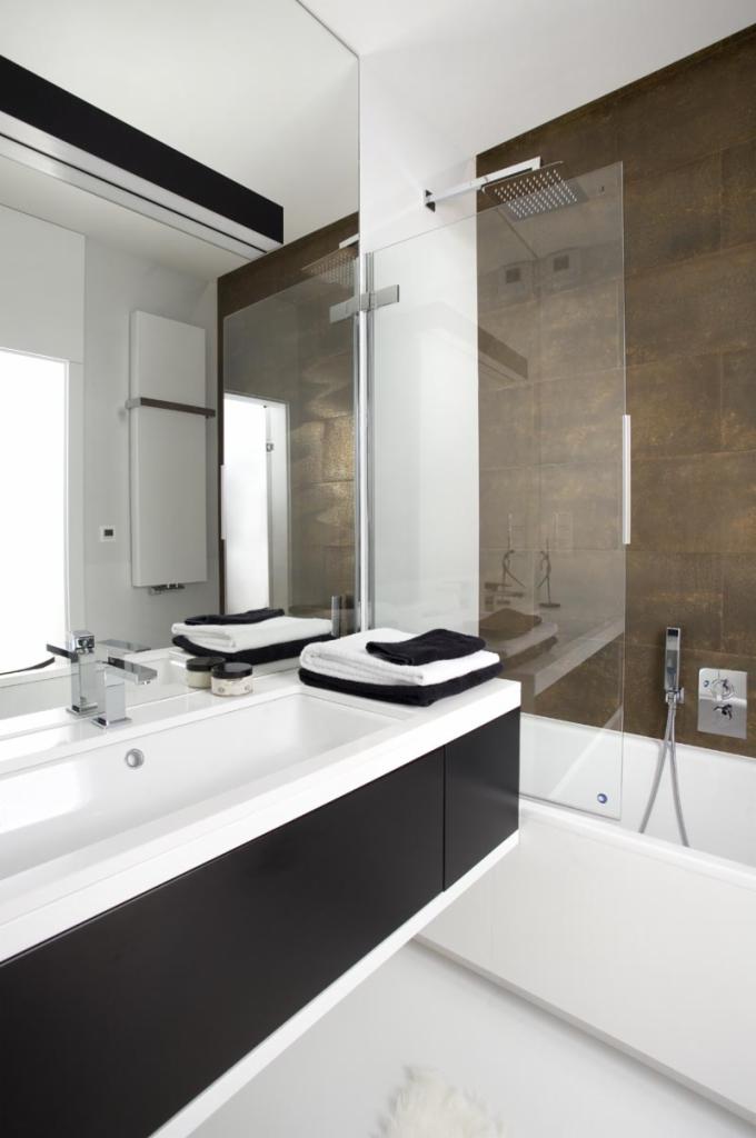 Nowoczesna łazienka z umywalką nablatową, czarnymi szafkami, szklanym panelem prysznicowym i brązowymi płytkami imitującymi kamień na ścianie.