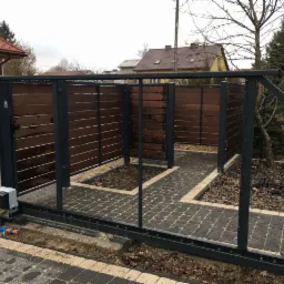 Automatyczna brama przesuwna z drewnianym wypełnieniem w kolorze orzecha, widoczny mechanizm otwierający, kostka brukowa przed bramą, dom w tle.