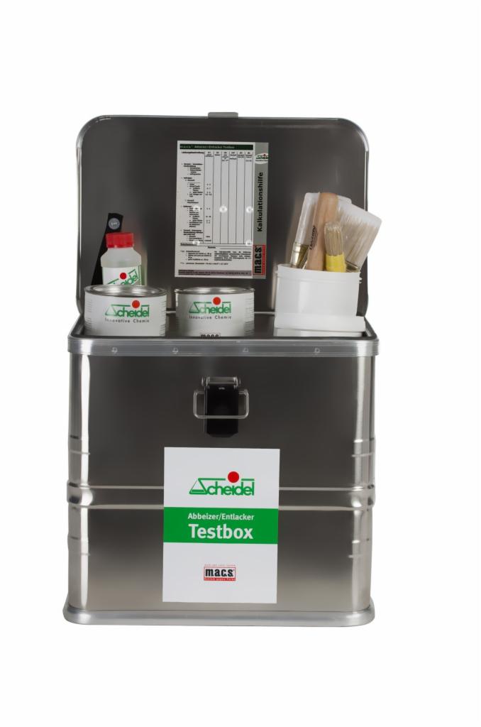Otwarta metalowa skrzynka testowa z widocznymi pojemnikami z chemikaliami Scheidel, pędzlami i dokumentacją, przeznaczona do usuwania powłok i lakierów.