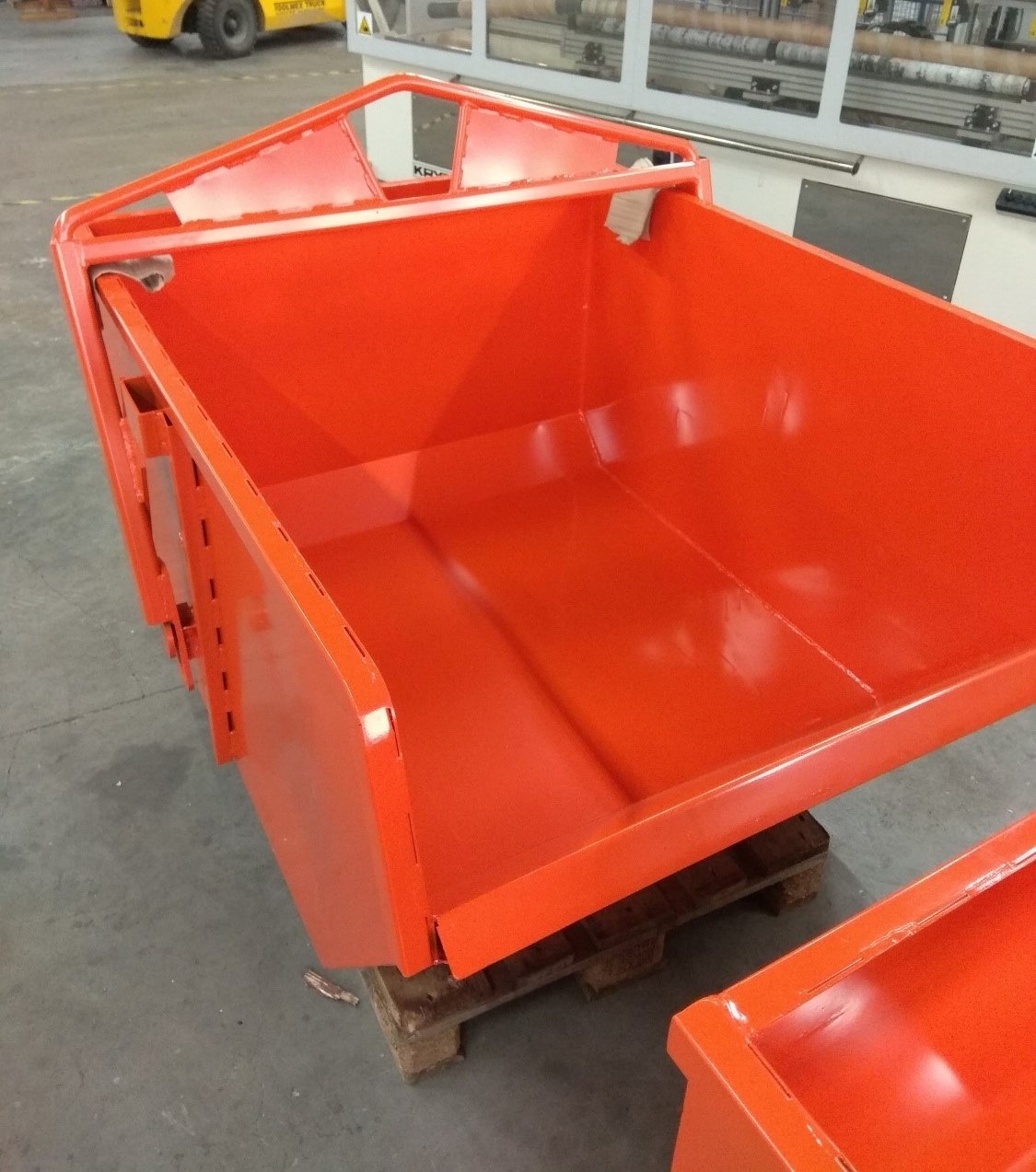 Pomarańczowy, metalowy kontener na palecie, widok z góry pod kątem, z widocznymi spawami i elementami mocującymi.