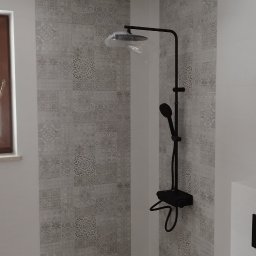 P.U. ELEWATOR MARIUSZ KOWALCZYK - Nowoczesna kabina prysznicowa z czarną armaturą i dekoracyjnymi płytkami ściennymi w odcieniach szarości, z drewnopodobną podłogą i odpływem liniowym.