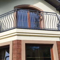 P.U. ELEWATOR MARIUSZ KOWALCZYK - Elewacja domu z beżową ścianą, brązowymi detalami okiennymi i ozdobnym, czarnym balkonem z metalowymi, zakrzywionymi prętami.