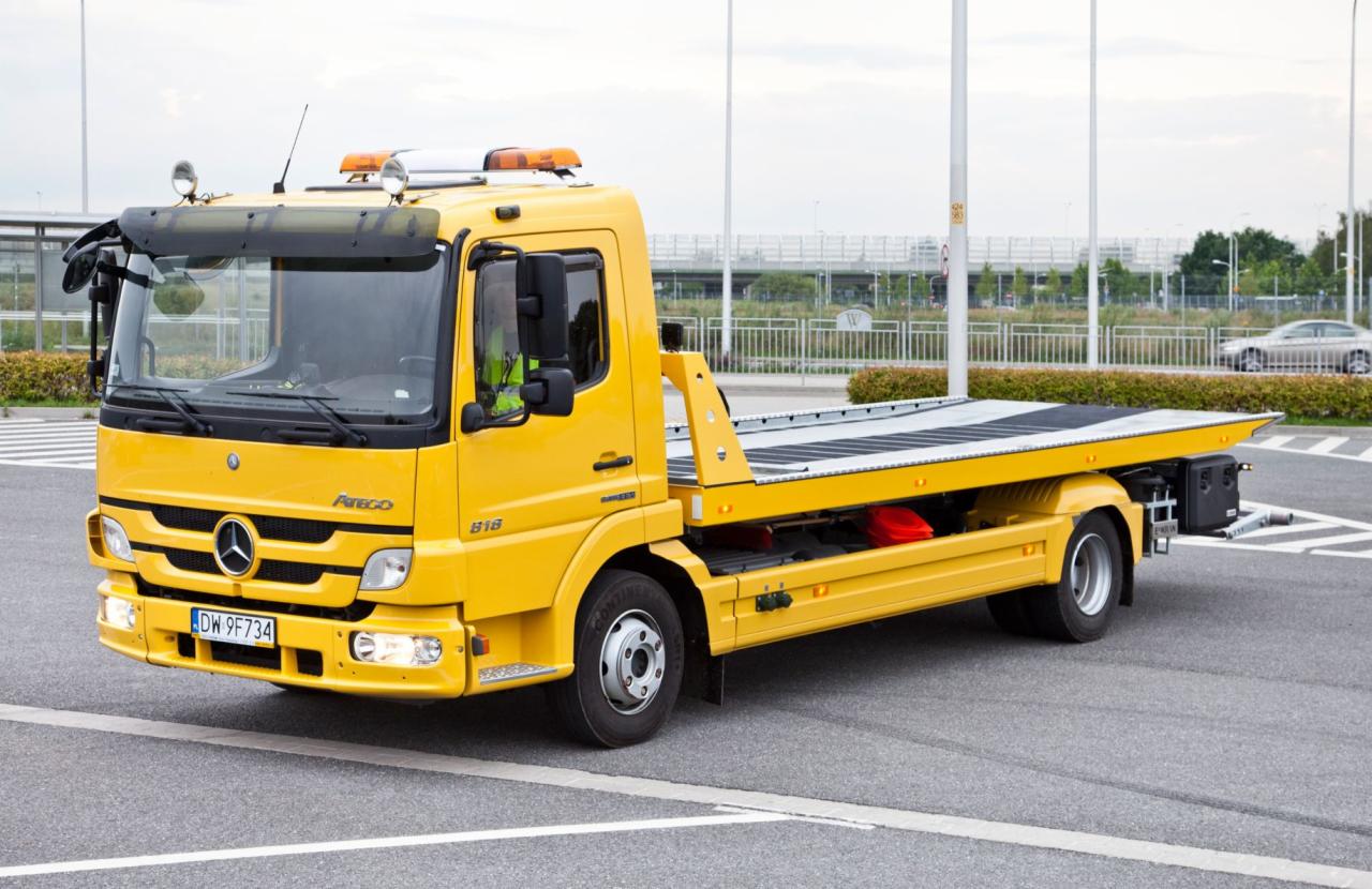 Żółta autolaweta Mercedes Atego 818 z włączonymi światłami, zaparkowana na parkingu we Wrocławiu, z widocznymi pomarańczowymi światłami ostrzegawczymi na dachu i tablicą rejestracyjną DW 9F734.
