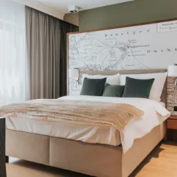 Nowoczesna sypialnia z łóżkiem kontynentalnym, wezgłowie ozdobione mapą Gdańska, minimalistyczne lampki nocne i drewniana szafka nocna.