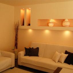 Zakład Remontowo Budowlany Piotr Kogut - Salon z beżowymi ścianami, wnękami z oświetleniem, kremową sofą i dekoracyjnymi poduszkami, minimalistyczny wystrój.