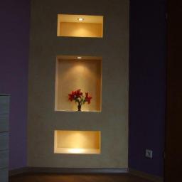 Zakład Remontowo Budowlany Piotr Kogut - Wnęki ścienne z oświetleniem punktowym, środkowa wnęka z wazonem czerwonych kwiatów na tle fioletowej ściany i komody