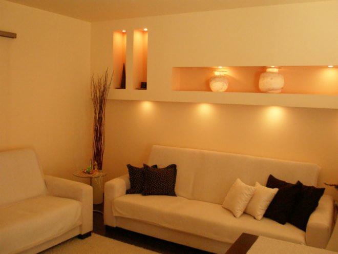 Salon z beżowymi ścianami, wnękami z oświetleniem, kremową sofą i dekoracyjnymi poduszkami, minimalistyczny wystrój.