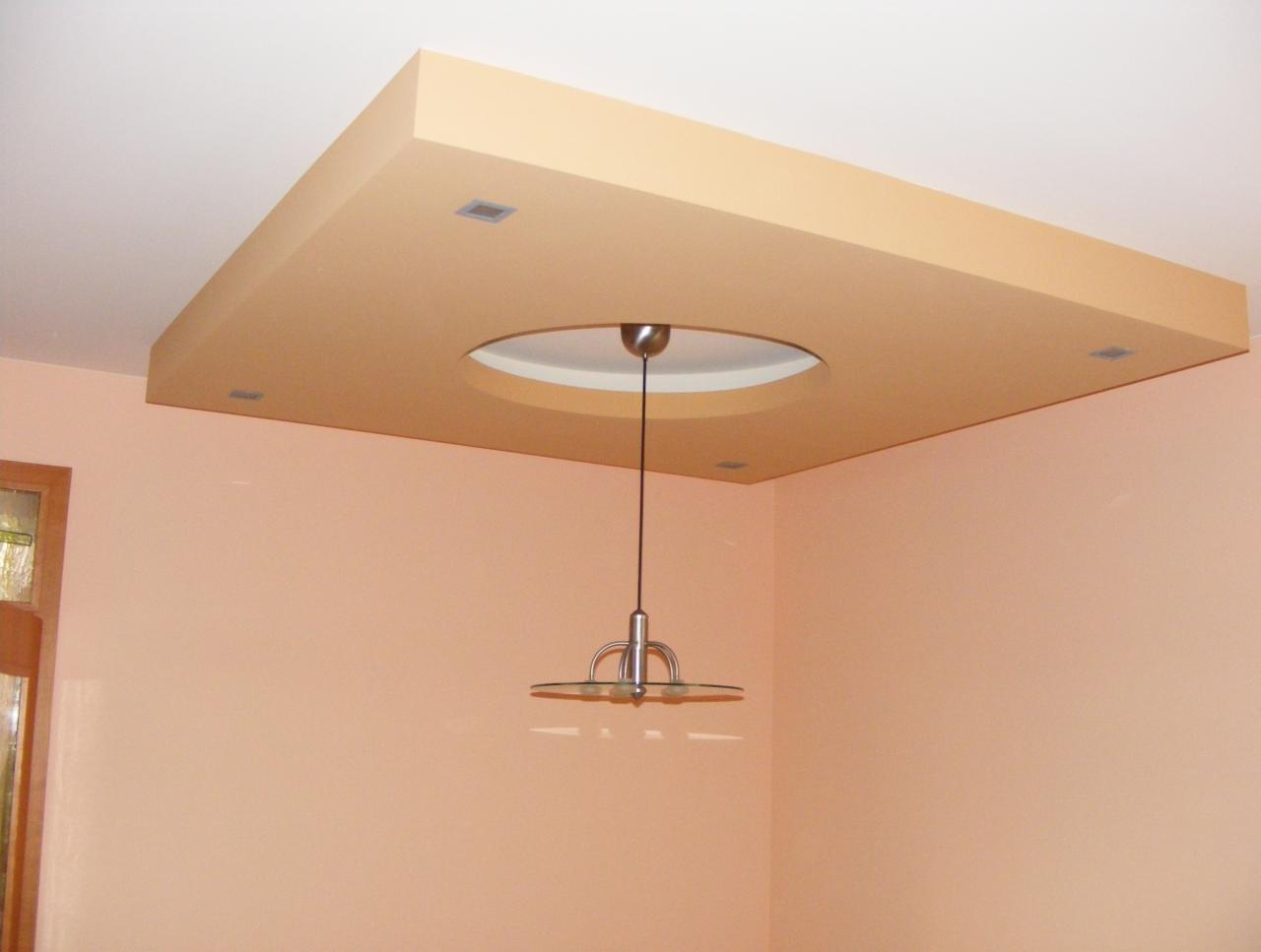 Kwadratowa zabudowa sufitowa z okrągłym otworem na lampę wiszącą, wbudowane halogeny, ściany w odcieniach brzoskwini.