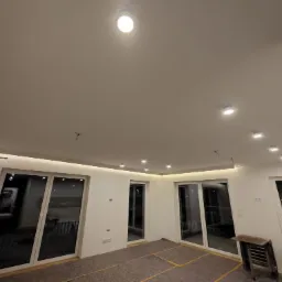 Pokój w trakcie remontu: białe ściany, przygotowane do gładzi, widoczne punkty oświetleniowe na suficie, zabezpieczona podłoga i drabina