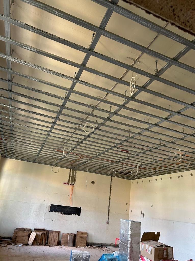 Montaż sufitu podwieszanego z płyt kartonowo-gipsowych, widoczne metalowe profile, płyty oraz instalacja elektryczna w pomieszczeniu w trakcie remontu.