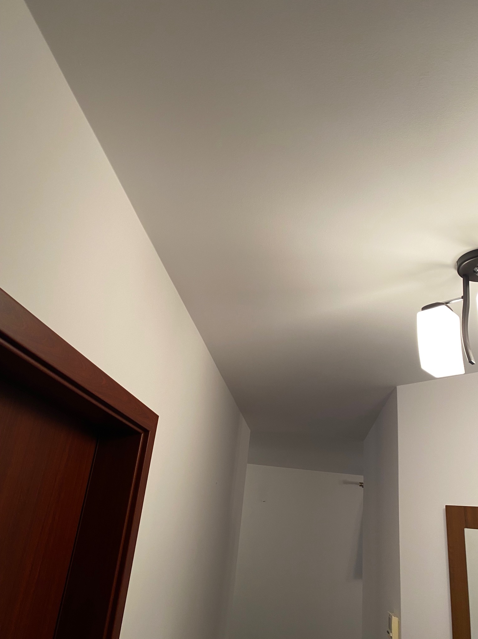 Fragment korytarza z widocznym sufitem po remoncie, oświetleniem i fragmentem drewnianej ościeżnicy drzwiowej.