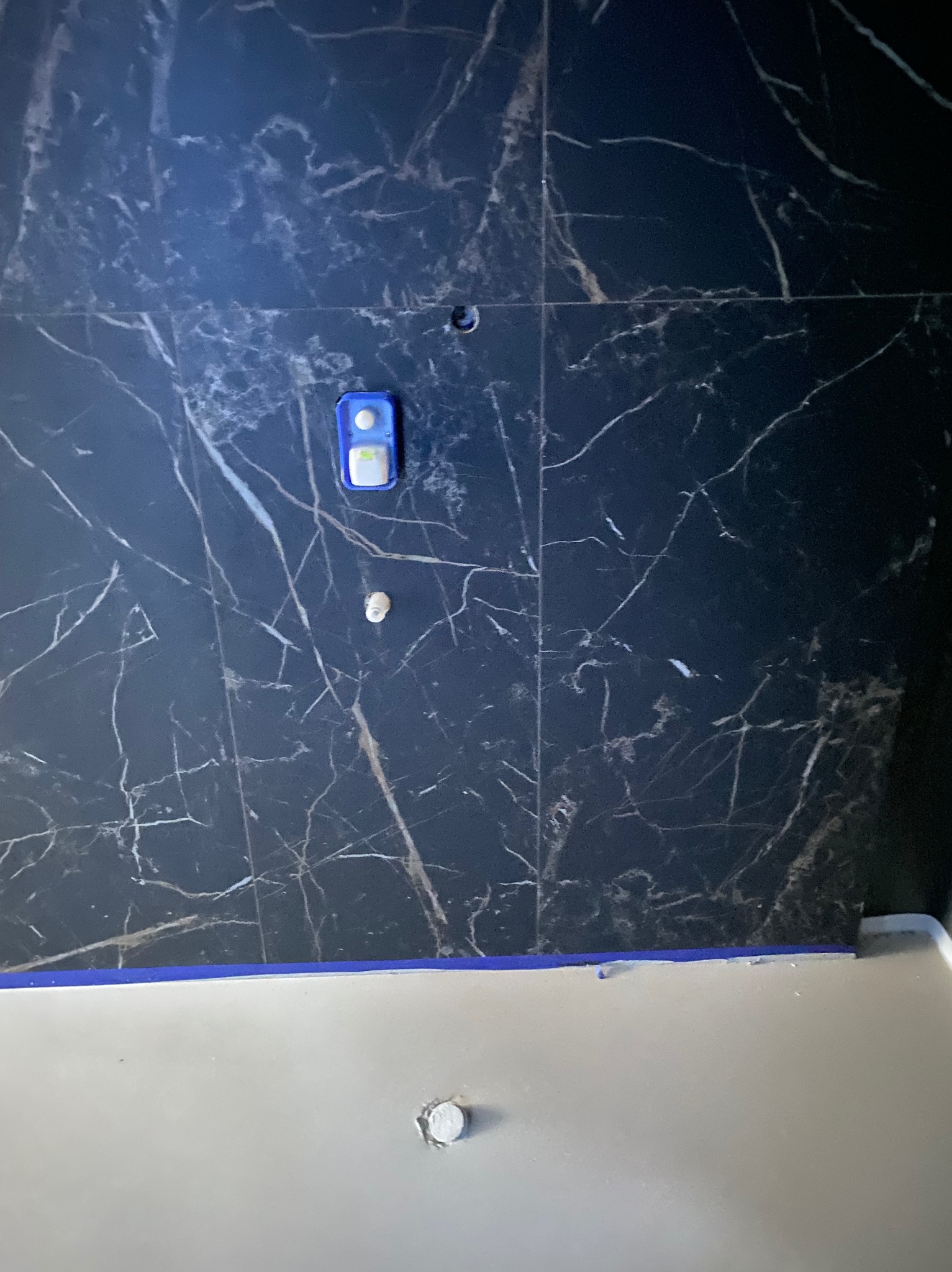 Ciemna ściana wyłożona płytkami imitującymi marmur z widocznymi elementami instalacji wodnej i fragmentem wanny, w trakcie prac wykończeniowych.