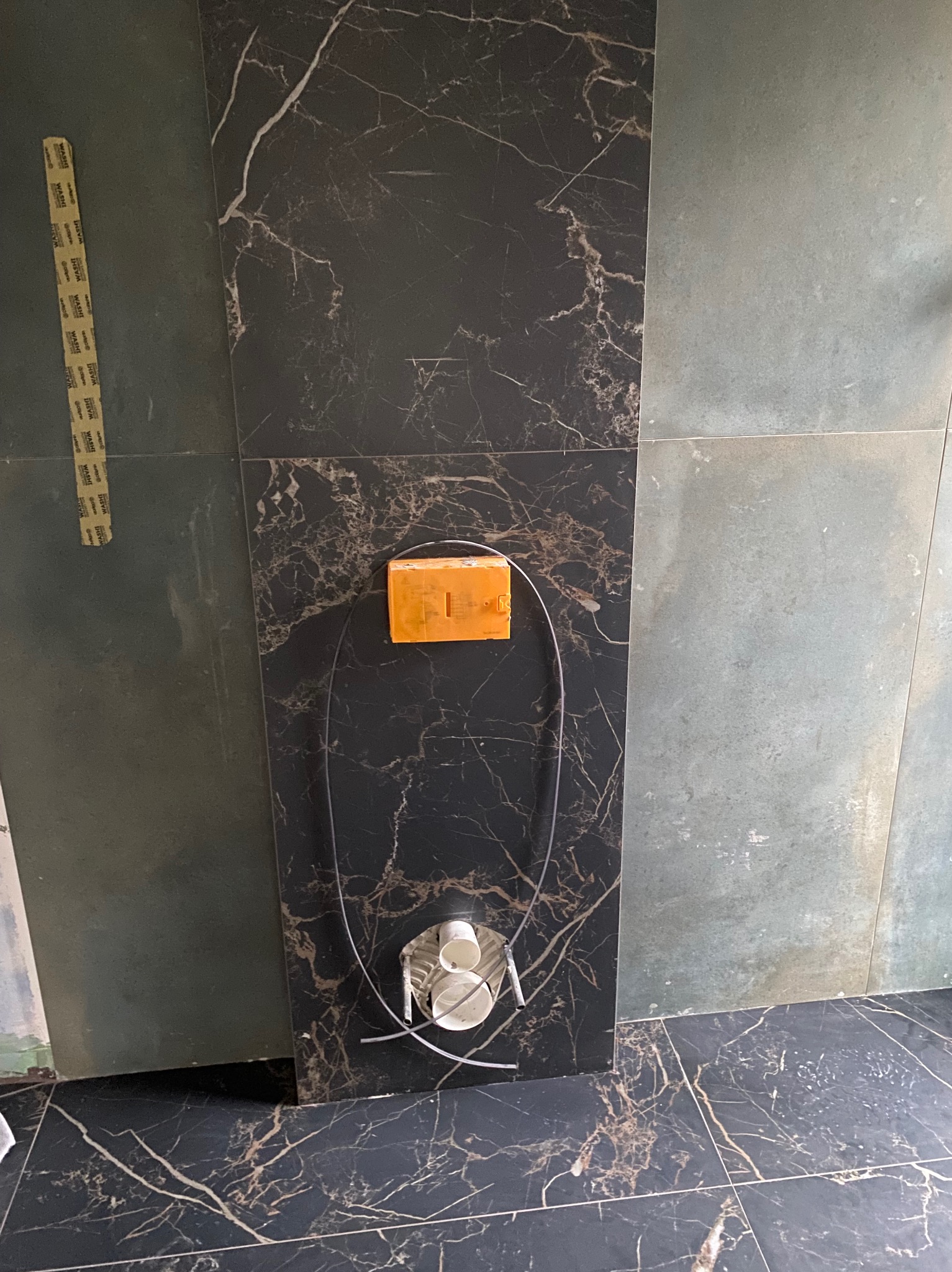 Montaż baterii podtynkowej na ścianie z płytek imitujących czarny marmur, widoczny fragment instalacji wodnej i narzędzia montażowe.