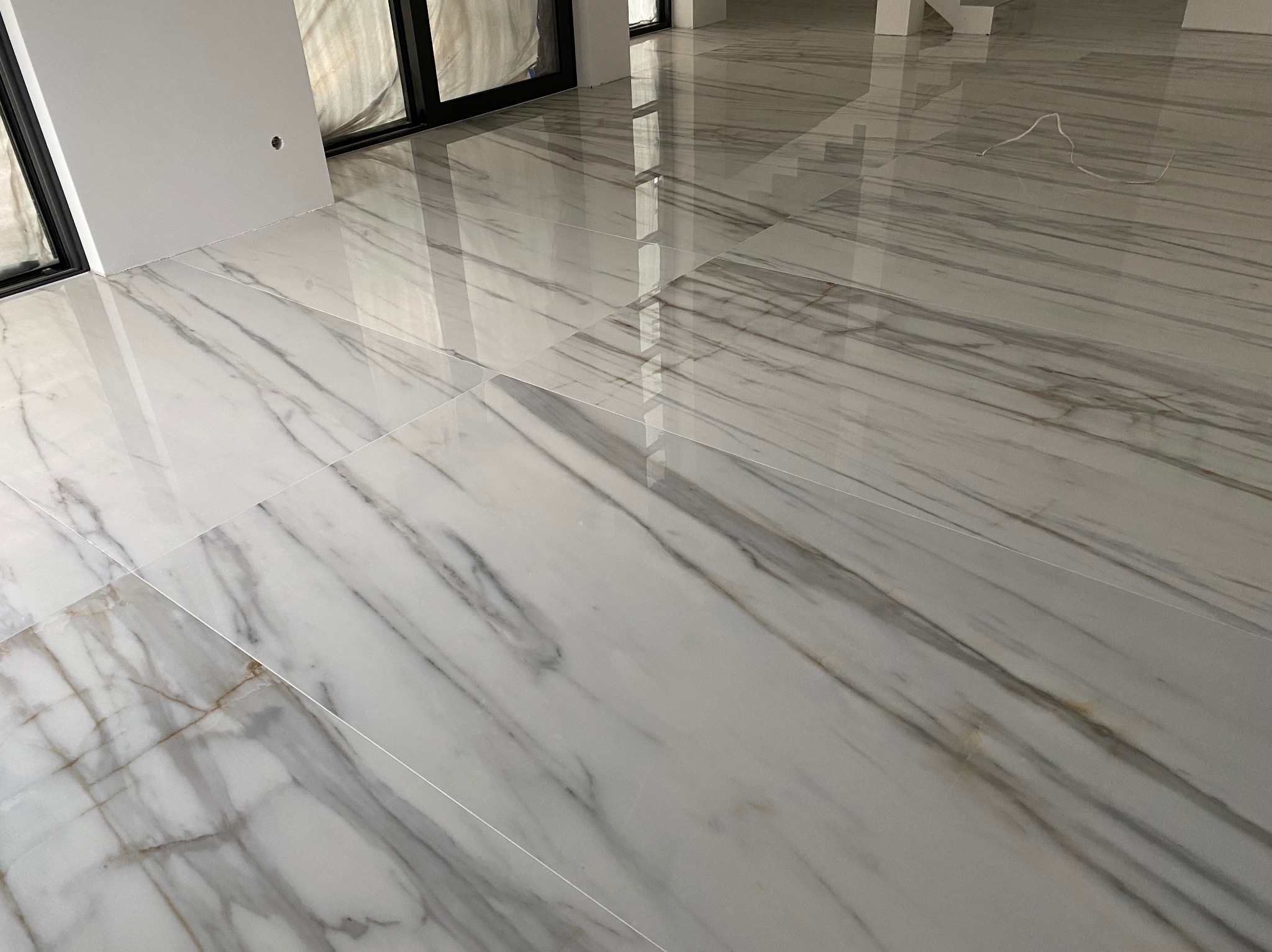 Błyszcząca, biała marmurowa podłoga ułożona w nowym, jasnym pomieszczeniu z oknami, odbijająca światło.