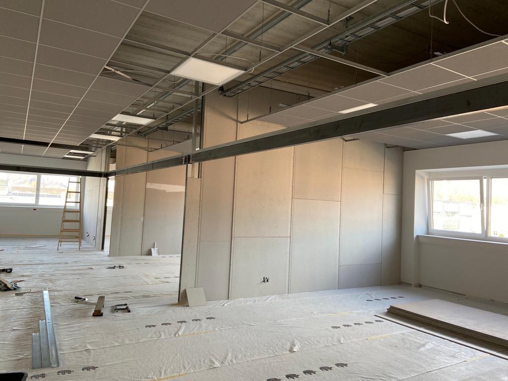 Montaż ścian działowych z płyt w nowym pomieszczeniu biurowym, widoczne profile stalowe, częściowo zamontowane płyty, zabezpieczona podłoga i drabina w tle.