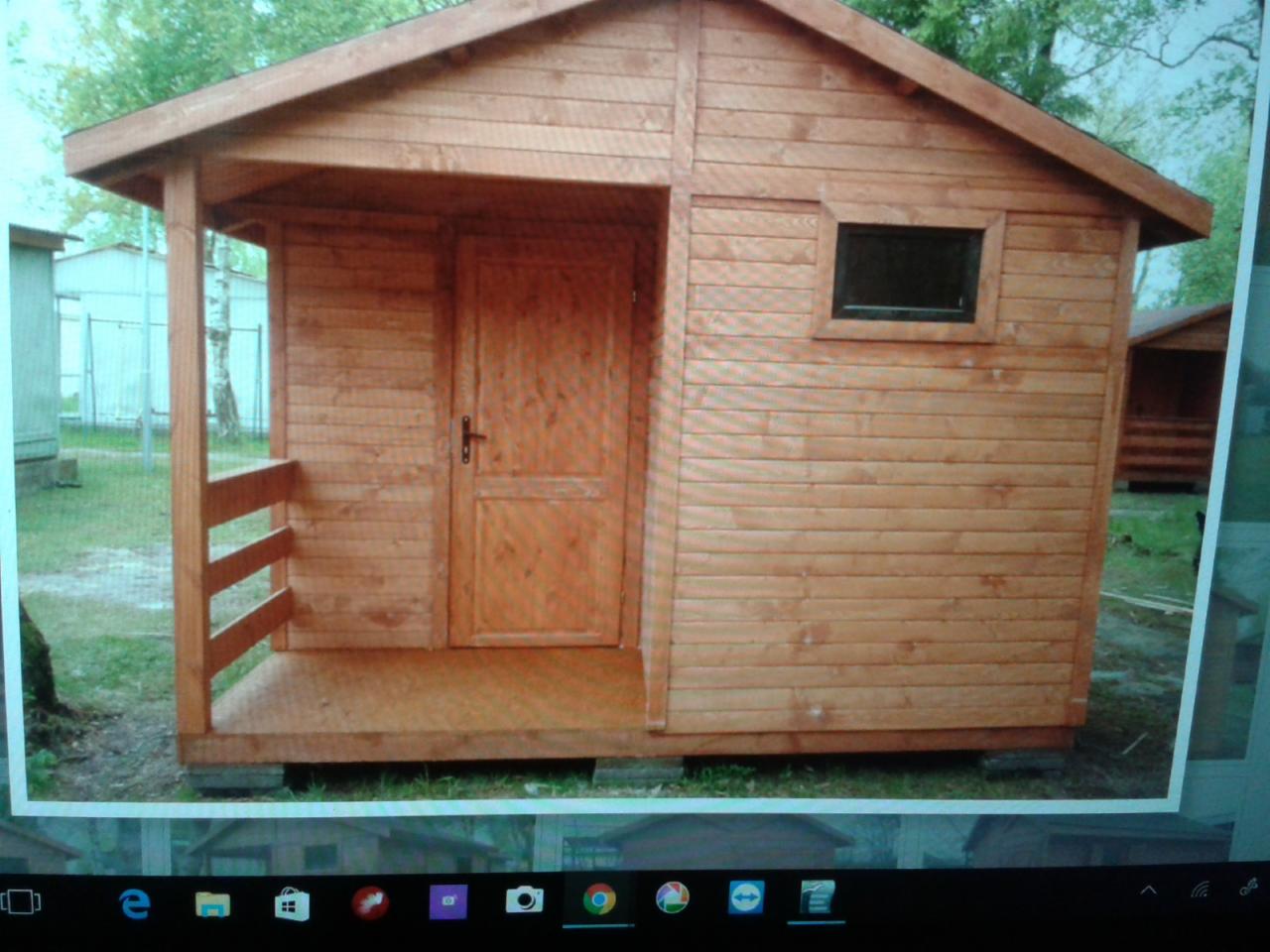 Mały, drewniany domek z prostokątnym oknem i zadaszonym wejściem, widoczny na tle zielonej trawy i drzew.